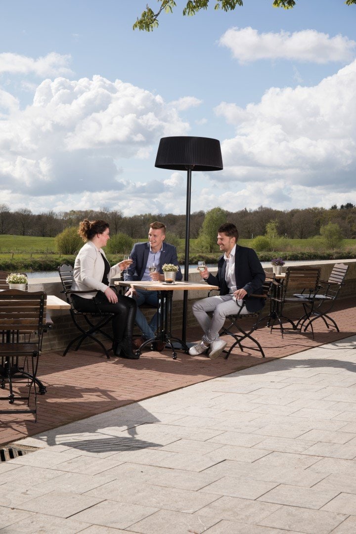Schwarzer Sunred Artix Terrassenheizstrahler auf Terrasse mit drei Personen.