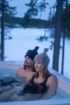 Zwei Menschen genießen ein Bad in einem Hot Tub in der Natur, umgeben von Bäumen und Schnee.