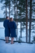 Zwei Frauen in dunkelblauen Bademänteln an einem Waldsee im Winter.